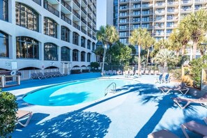 A swimming pool with lounge chairs and palm trees, surrounded by multi-story buildings. - WOW Newly Updated Ocean Front Condo with New Pools (North Myrtle Beach)