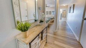 Um corredor com um aparador de madeira, plantas em vasos e um espelho.