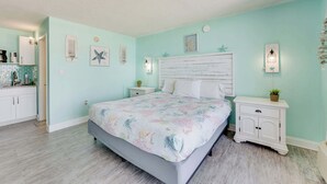 A bedroom with a bed, nightstands, a dresser, a window, and a kitchenette.
