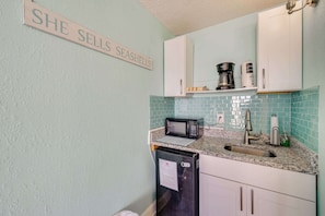 A kitchen with a sign that reads 'SHE SELLS SEASHELLS,' a microwave, a coffee maker, a sink, and cabinets. - New Honeymoon Studio @ Ocean Park,Ocean View,Pools (Myrtle Beach)