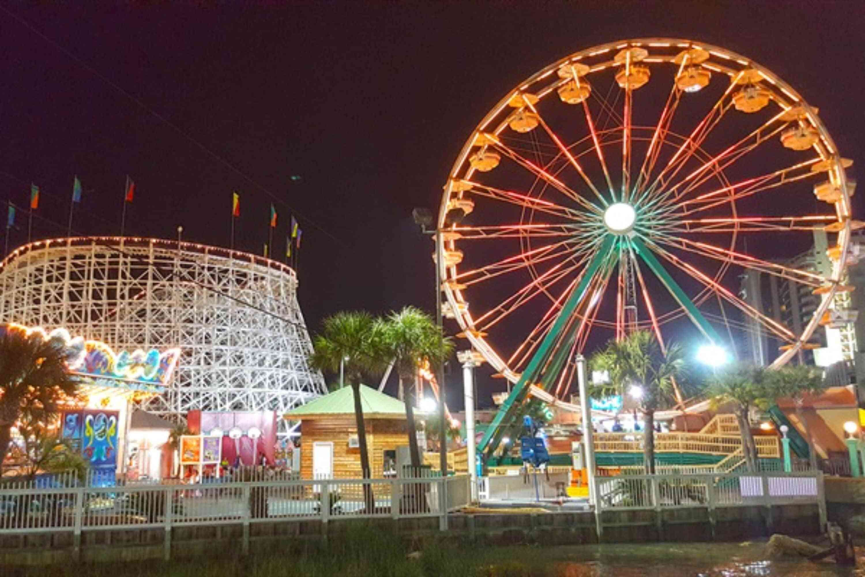A Ferris wheel and a roller coaster at a nighttime amusement park.