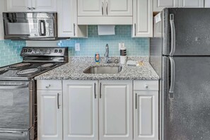 A kitchen with white cabinets, a stainless steel refrigerator, a microwave, and a stove.