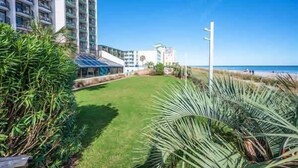 A hotel with a grassy lawn, palm trees, and a view of the beach and ocean. - Pets welcome,direct oceanfront, poolside,1 bedroom (Myrtle Beach)