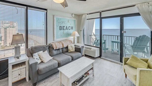 A modern living room with a grey sofa, a wooden coffee table, and a view of the beach through large windows. - Pets welcome,direct oceanfront, poolside,1 bedroom (Myrtle Beach)