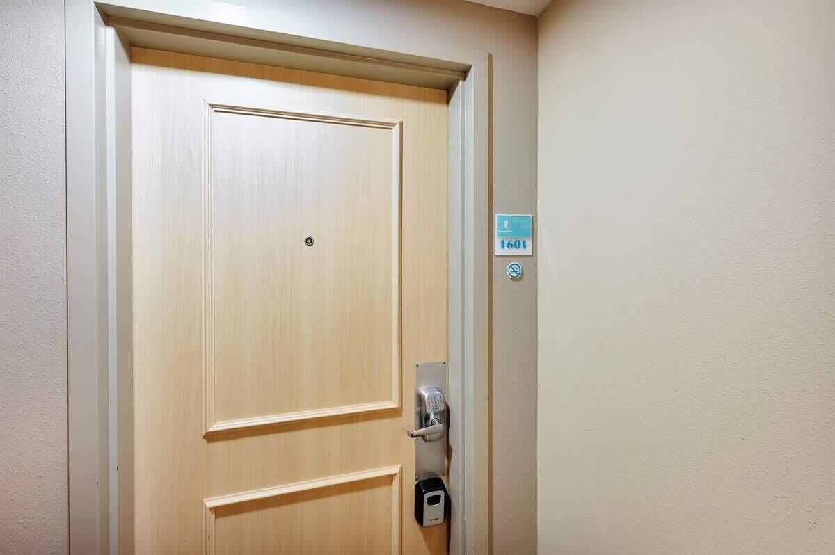 Una porta in legno con una serratura e un lettore di carte, una targa con il numero della stanza 1601 e un cartello che indica il divieto di fumare.