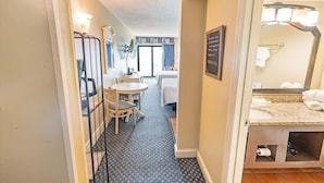 A hotel room with a bed, a small table with chairs, a desk, a chair, a bathroom with a sink and mirror, and a chalkboard with writing. - Oceanfront View w/ Beach Access at Sea Mist Resort (Myrtle Beach)