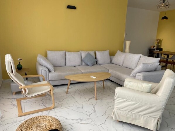 A living room with a grey sectional sofa, a wooden coffee table, a white armchair, and a wicker ottoman.