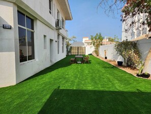 A white building with a small patio area featuring a table and chairs, surrounded by a well-maintained lawn.