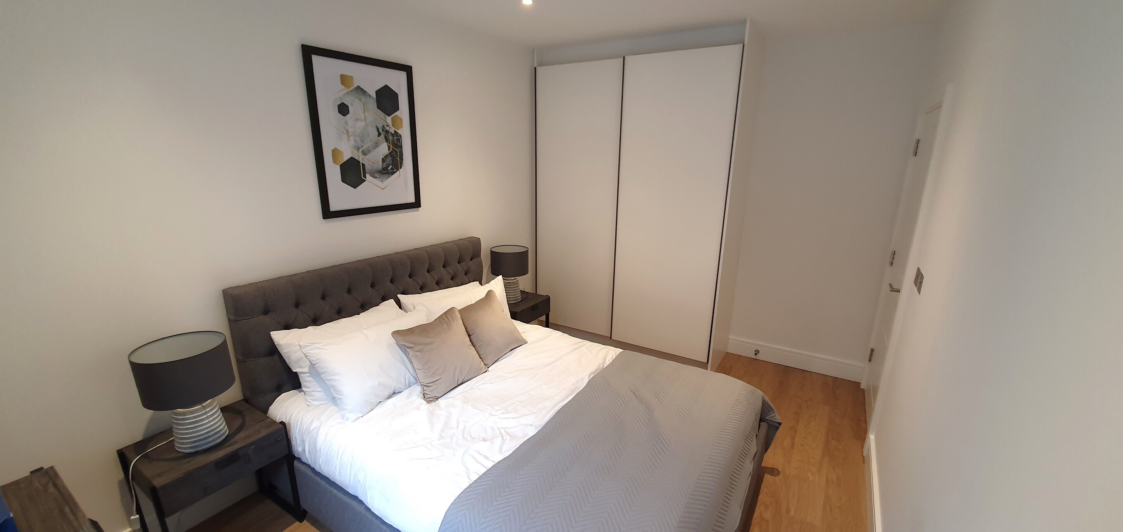 A bedroom with a bed, nightstands, a lamp, a wardrobe, and a framed picture on the wall.