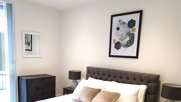 Een moderne slaapkamer met een groot bed, een hoofdbord, een nachtkastje, een lamp en een lijst met een afbeelding aan de muur.