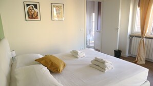 Quarto de hotel com uma cama, almofadas, toalhas e duas fotografias emolduradas na parede.