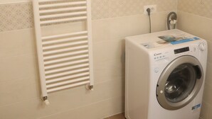 Uma área de lavandaria com um varal branco fixado na parede e uma máquina de lavar com abertura frontal.