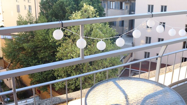 Varanda com cadeiras de vime e uma mesa de vidro, com vista para um horizonte urbano com edifícios e árvores.