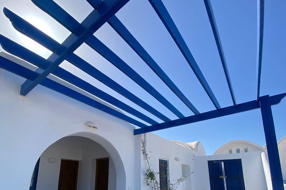 A covered outdoor area with blue beams, white walls, and a tiled floor.