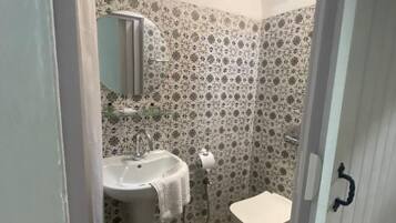 A small bathroom with a sink, toilet, and shower. The walls are tiled with a floral pattern.