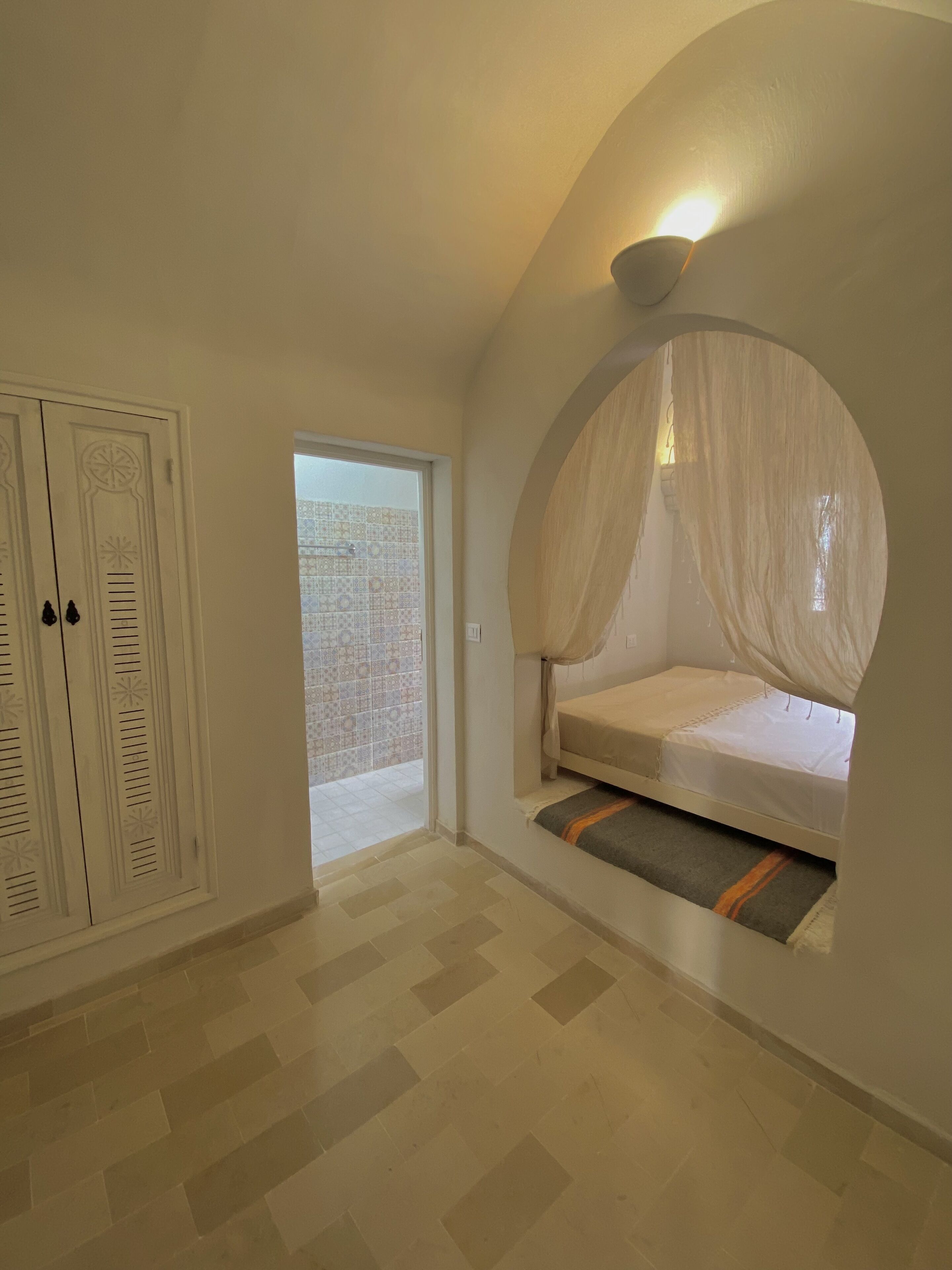 Una camera da letto con un letto a baldacchino, un armadio e vista su un balcone piastrellato.
