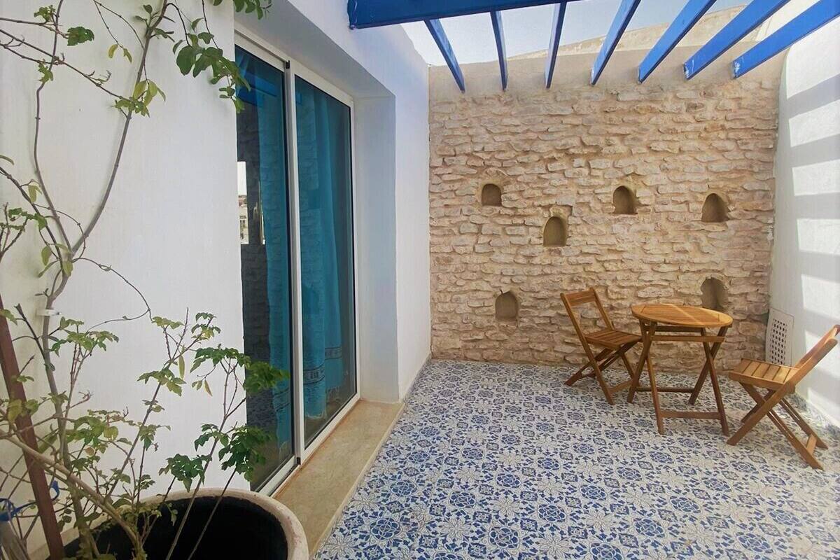 A patio with a stone wall, a blue pergola, a tiled floor, and a table with chairs.