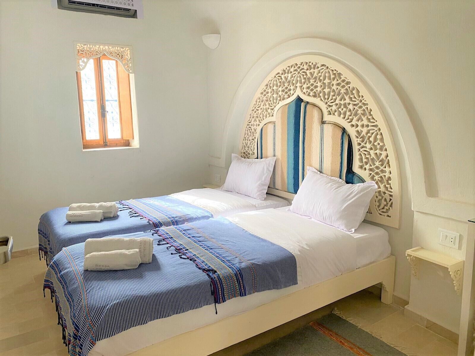Un lit double avec une couvre-lit à rayures et deux oreillers, une petite fenêtre avec un rideau et une tête de lit décorative.