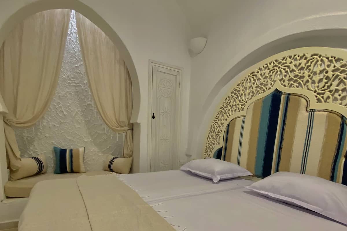 A neatly made bed with a striped headboard, a window with curtains, and a white door.