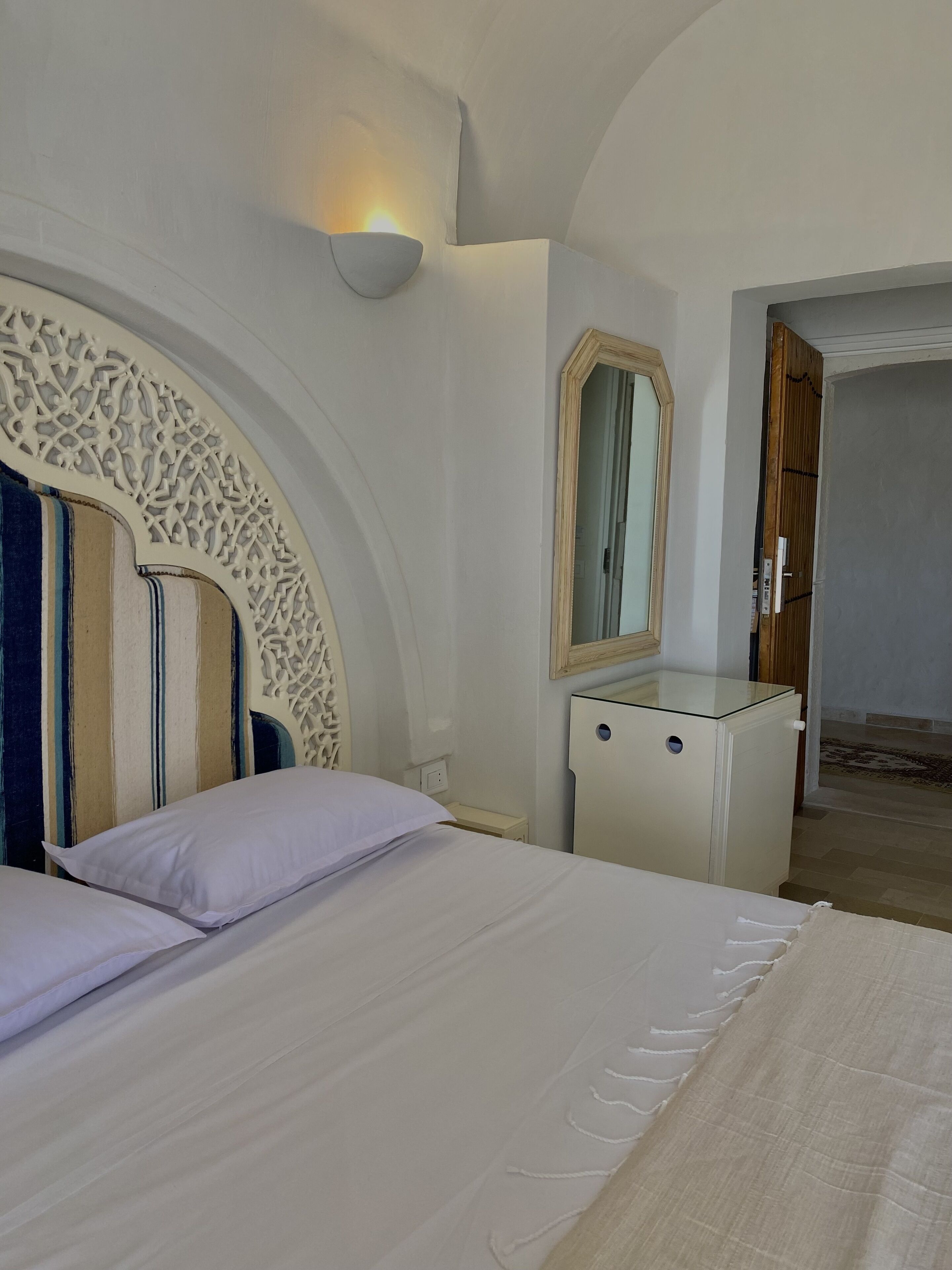 Une chambre à coucher avec un grand lit, une table de chevet, une commode, un miroir et un panneau décoratif mural.