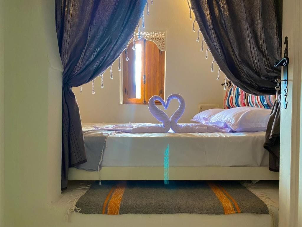 A bedroom with a bed, curtains, a heart-shaped light fixture, and a window.