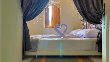 A bedroom with a bed, curtains, a heart-shaped light fixture, and a window.