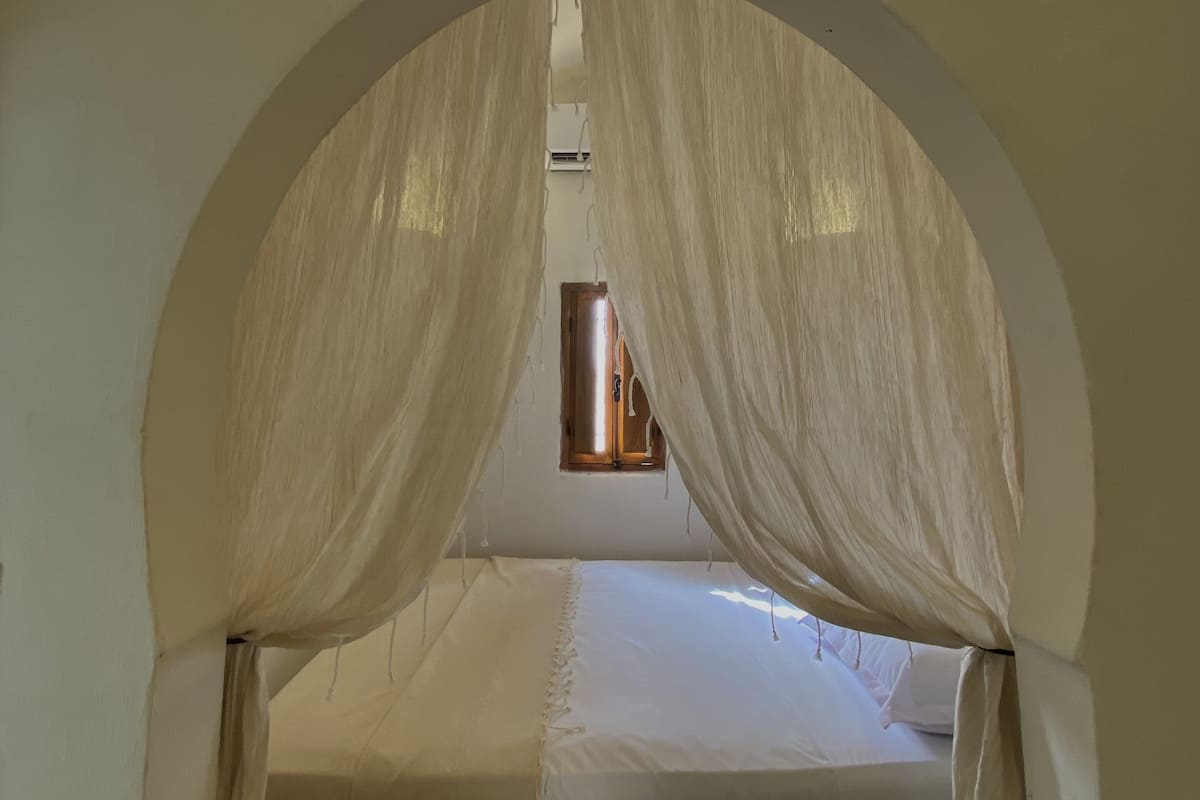 A bedroom with a bed under an arched ceiling, a window, and a light fixture.