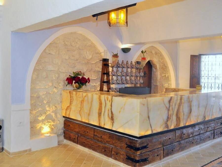 Un área de recepción con mostrador de mármol, arcos de piedra y una estantería para plantas en la pared.