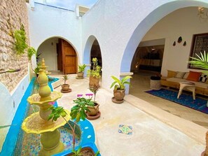 Stroll through a tranquil courtyard with a soothing fountain, surrounded by lush greenery and a beautifully tiled floor.