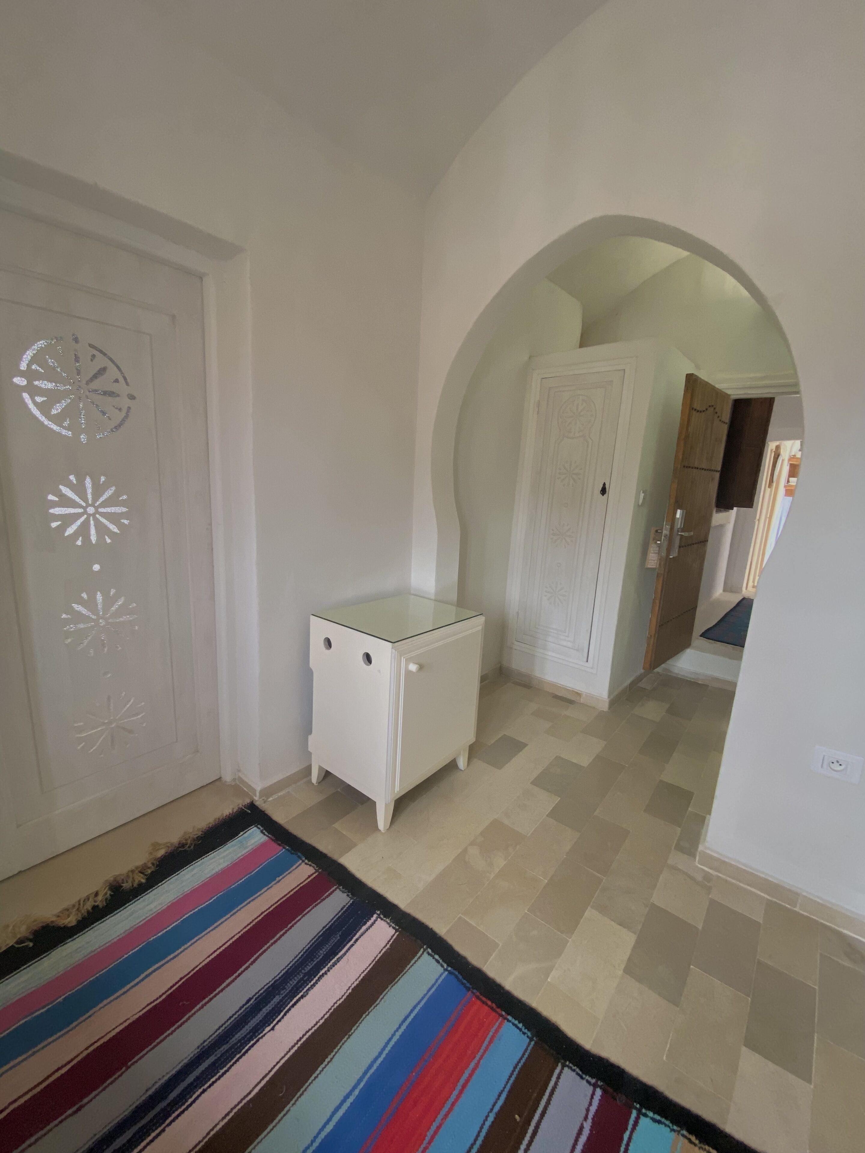 A hallway with a white door, a small white table, and a colorful striped rug.