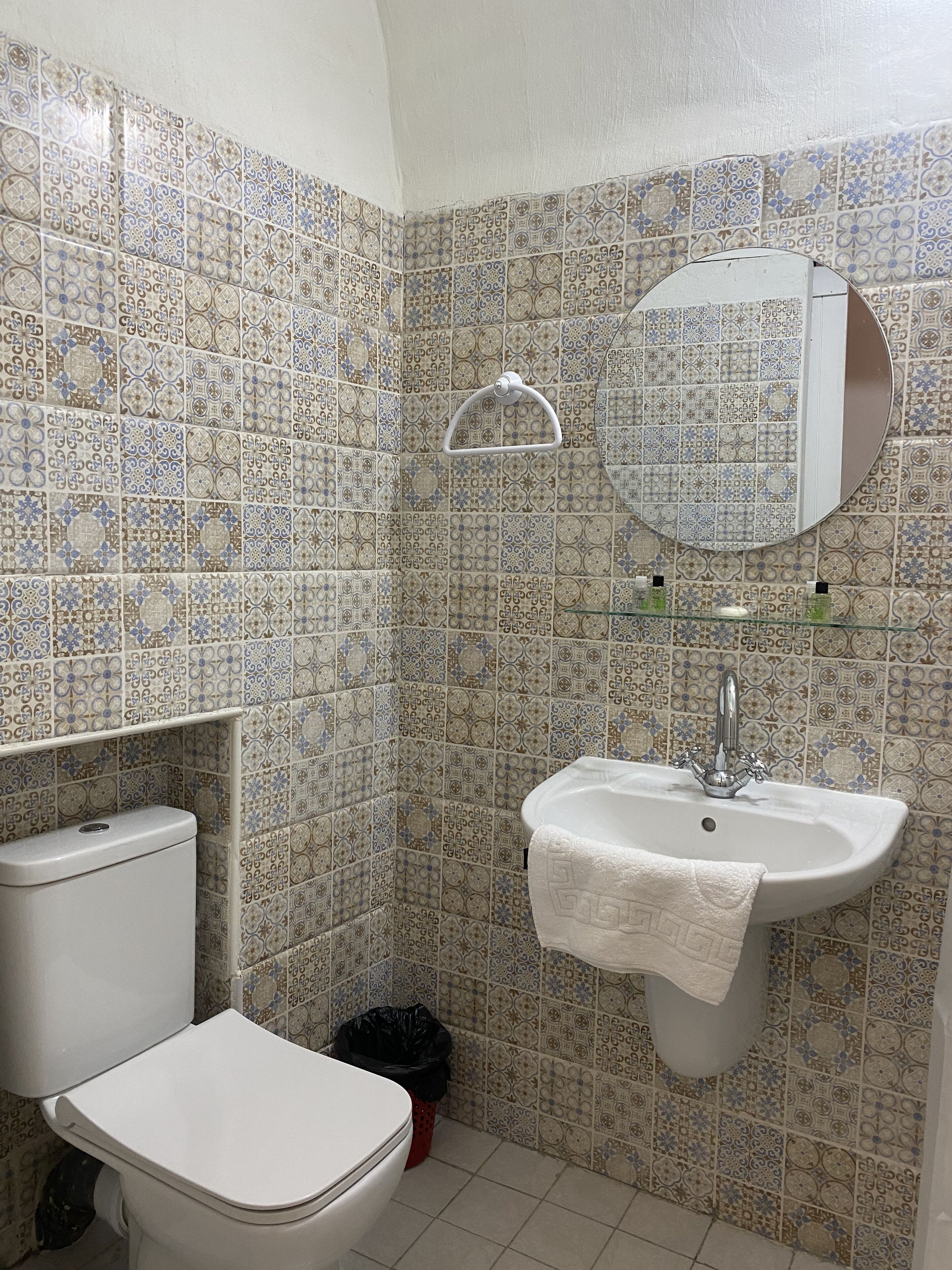 A bathroom with patterned tiles, a toilet, a sink with a mirror, and a towel rack.