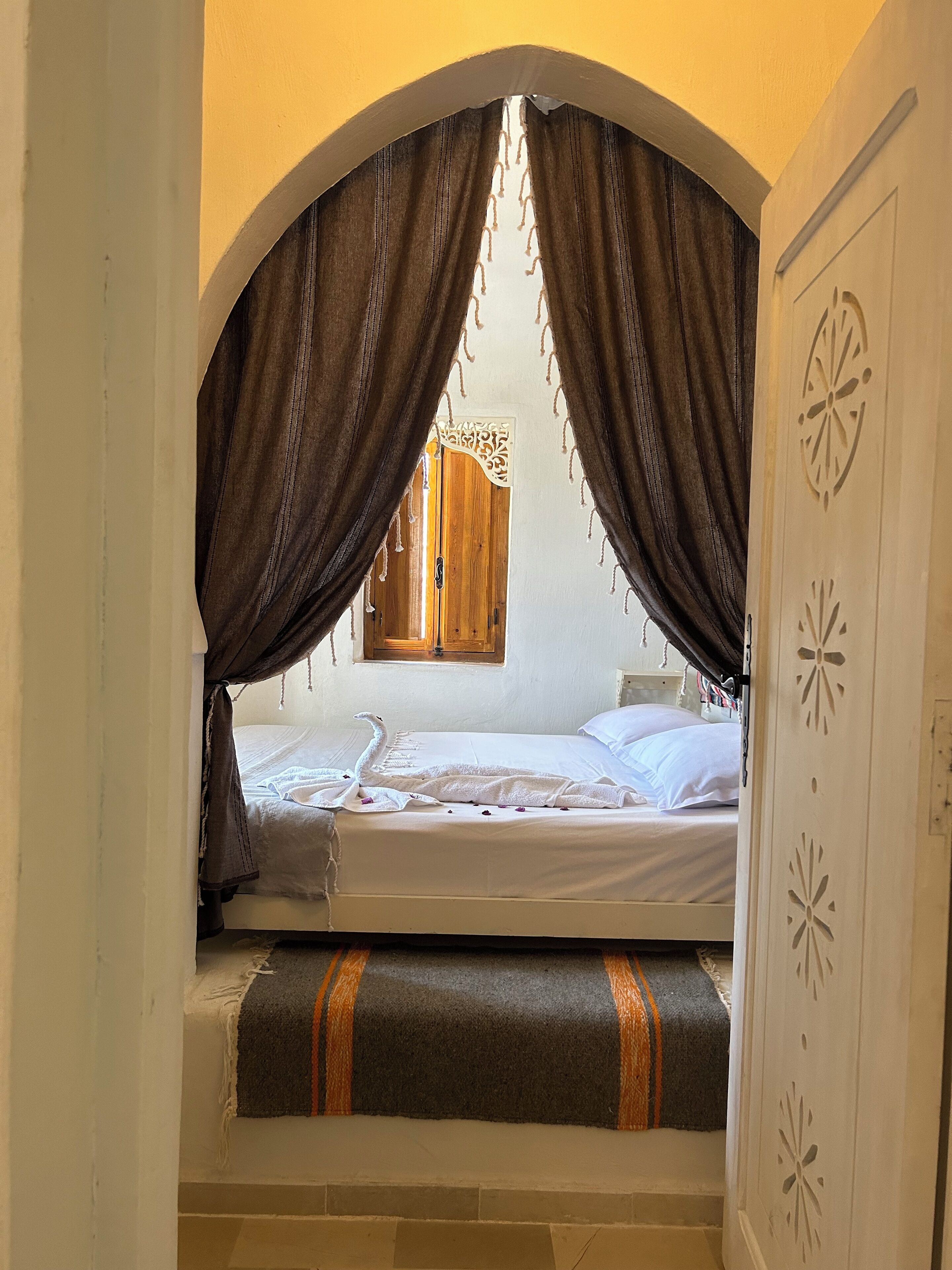 Una habitación con cama, cortinas, una puerta de madera y una ventana.