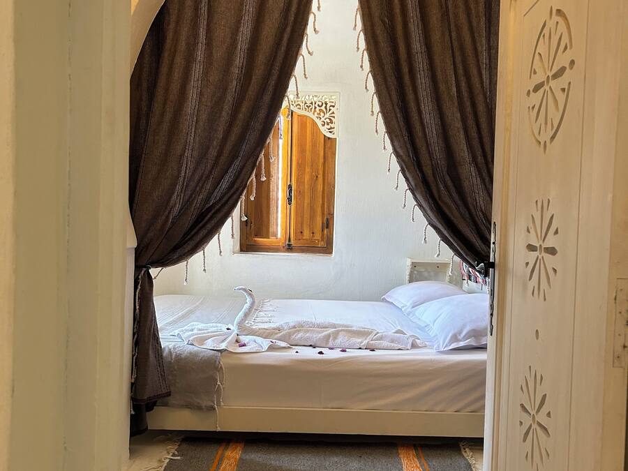 Una habitación con cama, cortinas, una puerta de madera y una ventana.