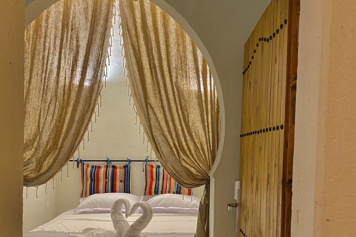 A bedroom with a bed, curtains, and a wooden door.