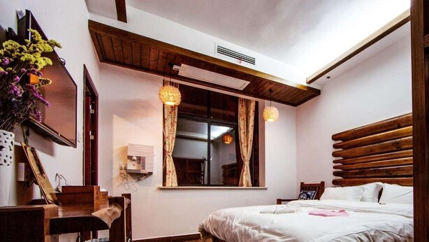 Ein Schlafzimmer mit einem Holz-Kopfteil, einem Bett mit weißer Bettwäsche, einem Fenster mit Vorhängen und einem Holzstuhl.