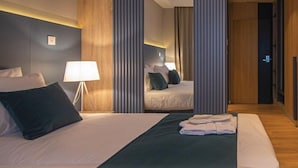 A hotel room with a large bed, a bedside table with a lamp, a mirror, and a view of the hallway. - Kalima resort (Mostar)