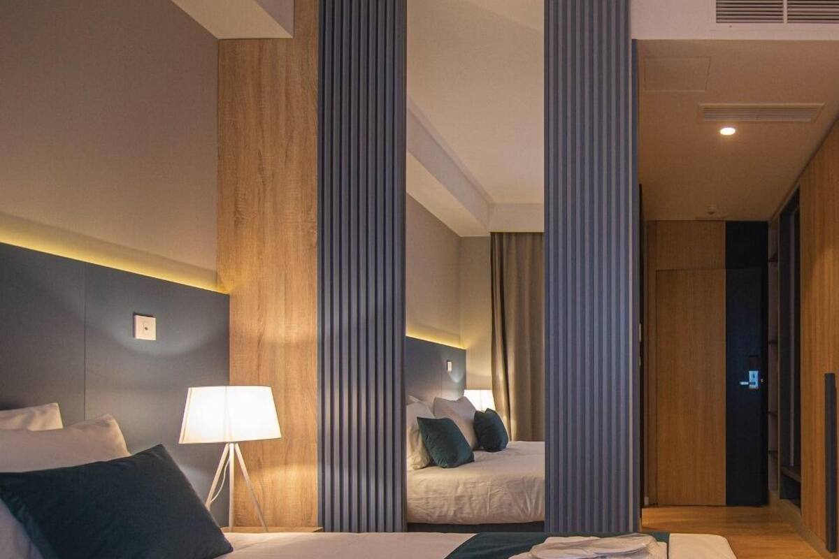 Une chambre d’hôtel avec un grand lit, une table de chevet avec une lampe, un miroir et une vue sur le couloir.