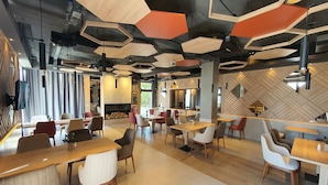 A modern restaurant interior with hexagonal ceiling panels, wooden tables, and chairs. - Kalima resort (Mostar)