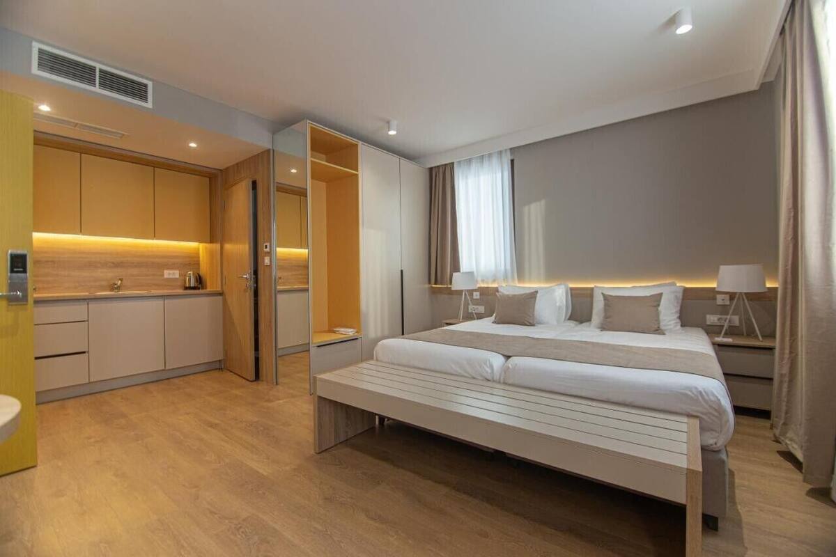 Une chambre d’hôtel moderne équipée d’un lit, de tables de chevet, d’une armoire intégrée et d’une kitchenette.