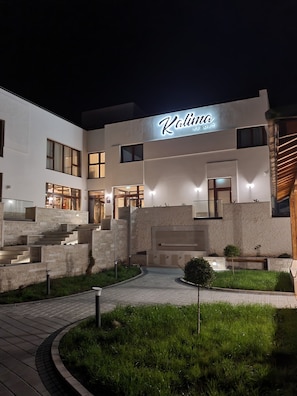 A modern building with a sign reading "Kalina Resort". It features a multi-level entrance with steps and a pathway leading to the main entrance.