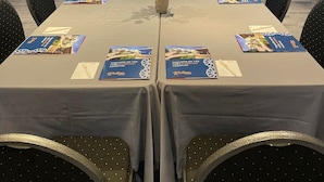 A conference room with a long table, chairs, a projector screen, and a floral centerpiece. - Kalima resort (Mostar)