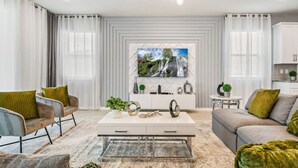 A modern living room with a sofa, armchairs, a coffee table, and a TV mounted on the wall.