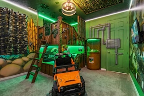 Habitación temática de selva, con una escalera, un jeep de juguete y una pared verde con una puerta.
