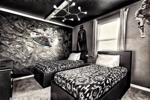 A bedroom with two beds, a stone wall mural, a Darth Vader figure, and a Star Wars helmet.