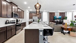 A modern kitchen with dark wood cabinets, a central island, and a hanging pendant light.