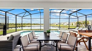 A covered outdoor area with a pool, lounge chairs, and a table with chairs.