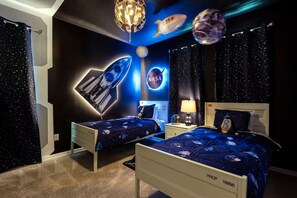 A bedroom with two beds, a NASA-themed wall, and a ceiling with space-themed decorations.
