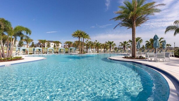 A large, clear swimming pool surrounded by palm trees and lounge chairs.
