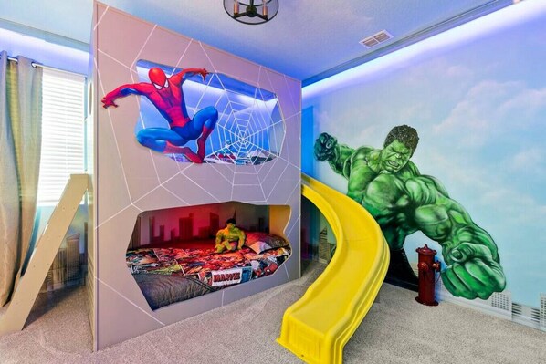 A child's bedroom with a bed, a slide, and a wall mural of a superhero.
