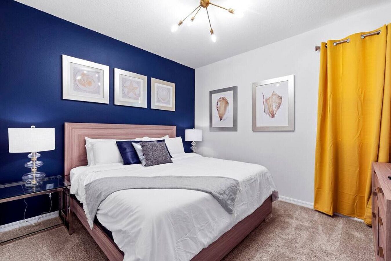 A bedroom with a bed, bedside tables, a headboard, and framed artwork on the walls.